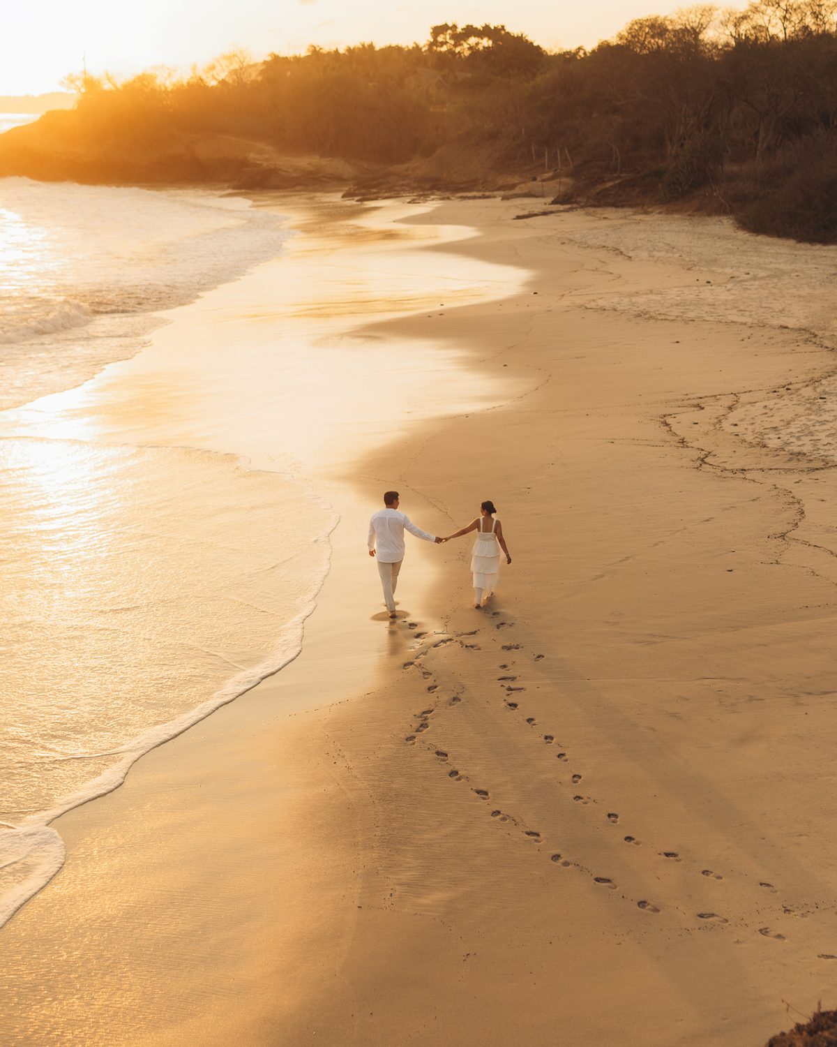 Couple walking hand in hand on an empty beach at sunset