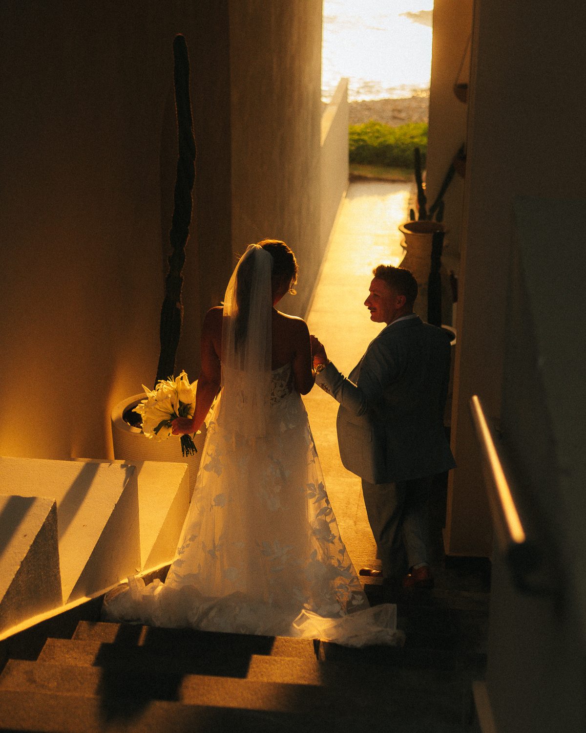 Bride and groom walking down golden-lit stairs toward the sea
